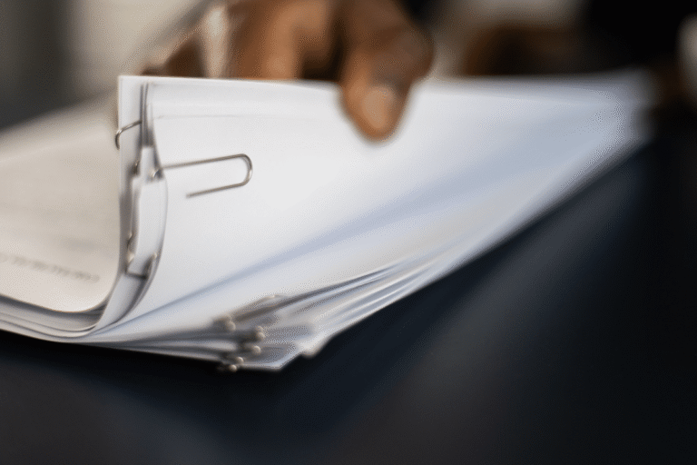 Documents empilés avec un trombone, main en arrière-plan.