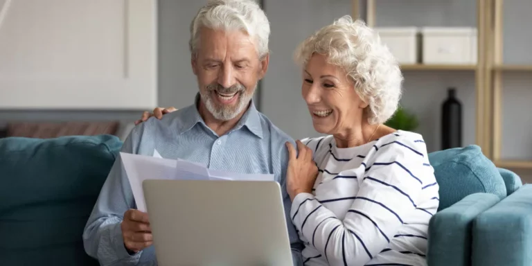 Couple âgé riant ensemble devant un ordinateur portable.