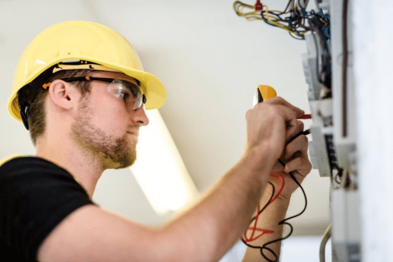 Technicien électricien utilisant un multimètre sur un tableau électrique.