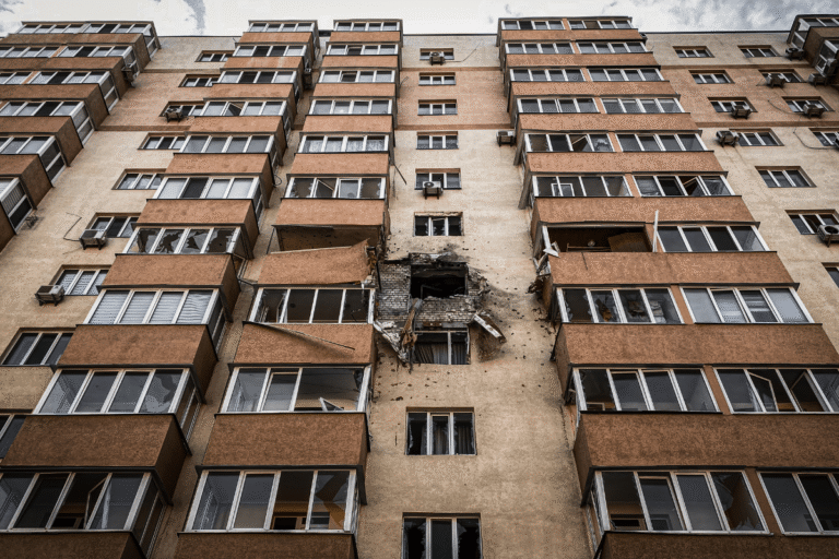 Façade d'immeuble avec un gros impact et fenêtres brisées.