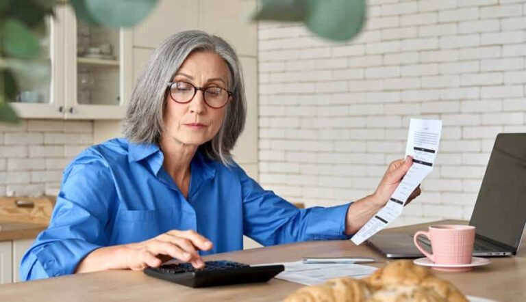 Femme âgée avec des lunettes utilisant une calculatrice et tenant un reçu.