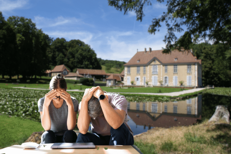 Couple assis, la tête entre les mains, devant un château et un lac.