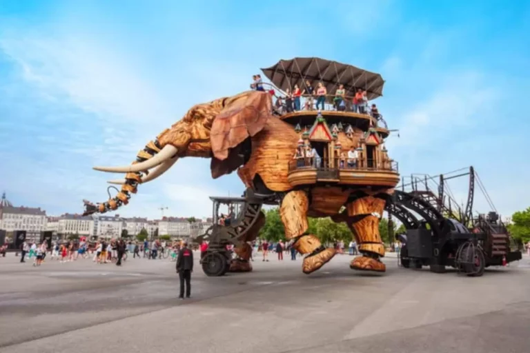 Éléphant mécanique en bois avec passagers, devant une foule.