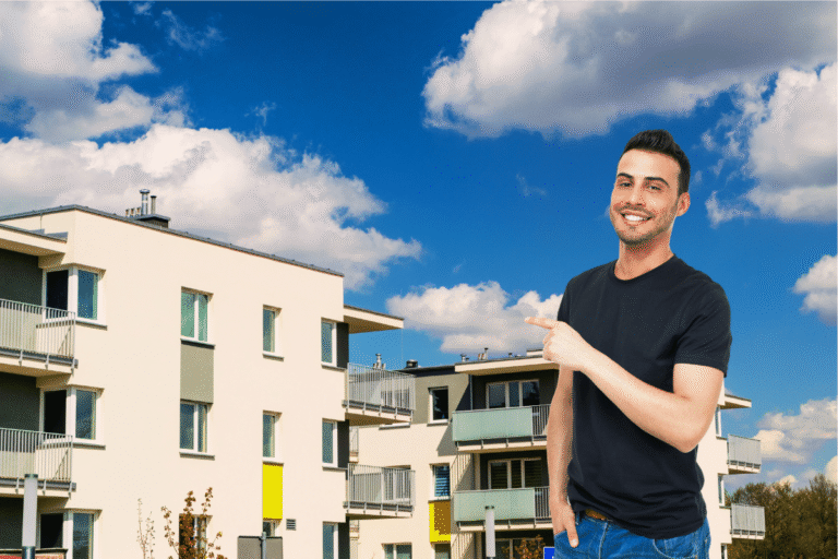 Homme souriant montrant un bâtiment moderne sous un ciel nuageux.