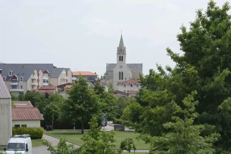 Église avec clocher entourée d'immeubles et arbres.
