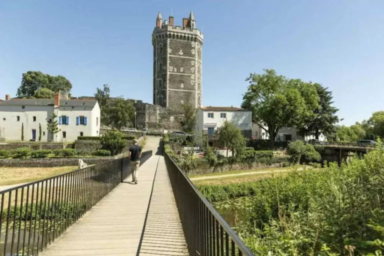 Tour médiévale surplombant un jardin verdoyant et un pont.