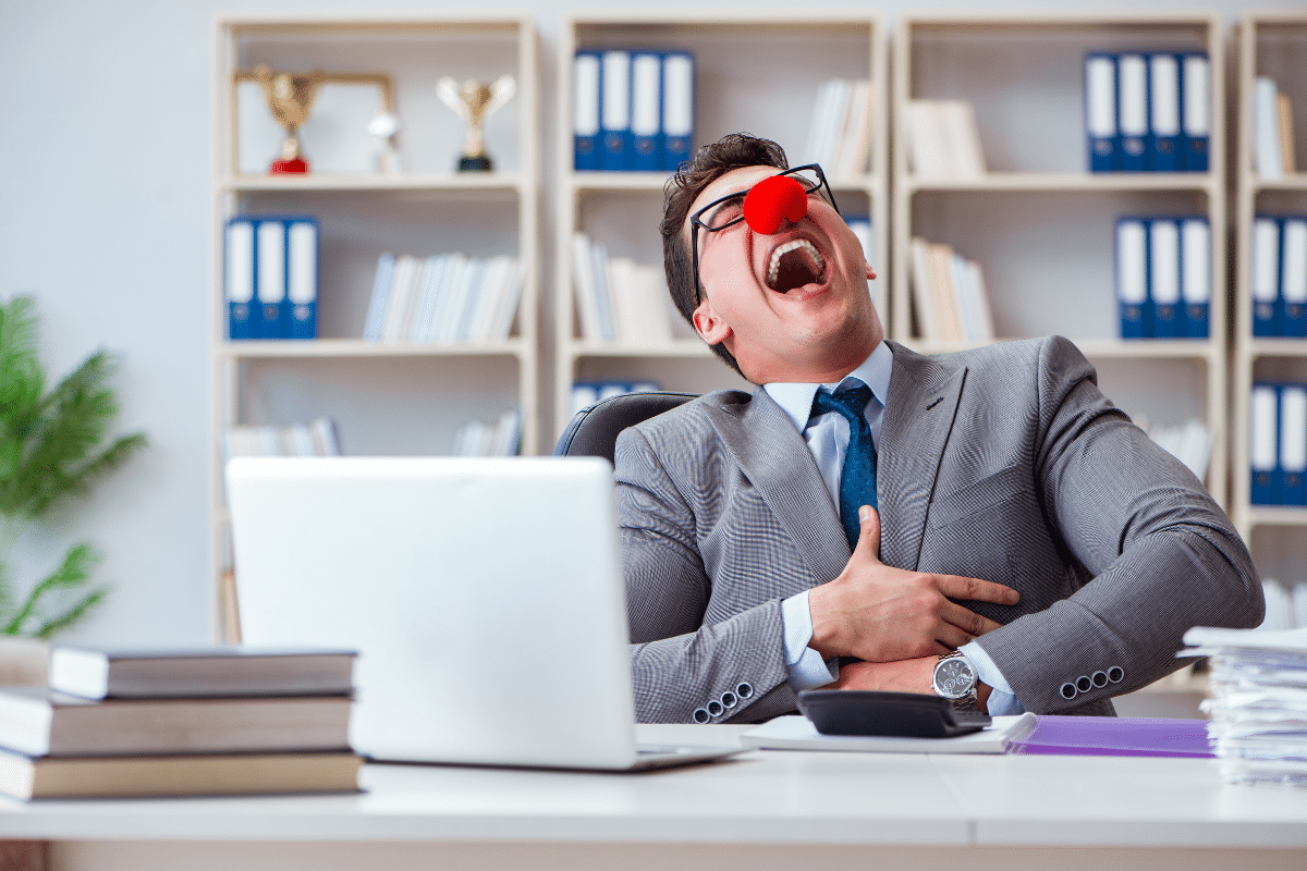 Homme en costume riant avec un nez de clown au bureau.