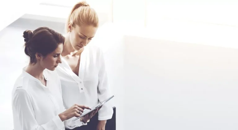 Deux femmes en chemises blanches regardent une tablette.
