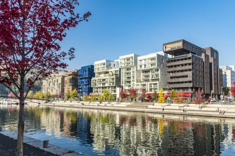 Bâtiments modernes au bord d'un canal, arbres colorés.