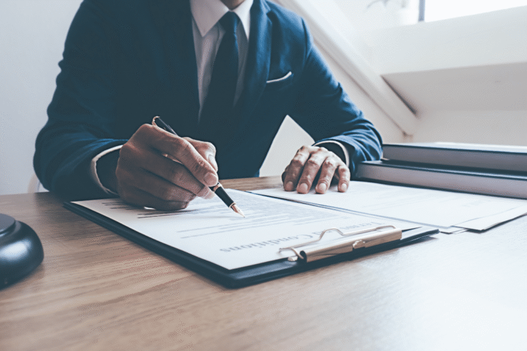 Homme en costume signant un document sur bureau.