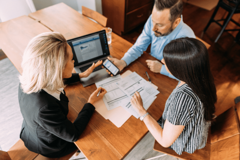 Trois collègues discutent autour d'une table, avec des documents et un ordinateur portable.