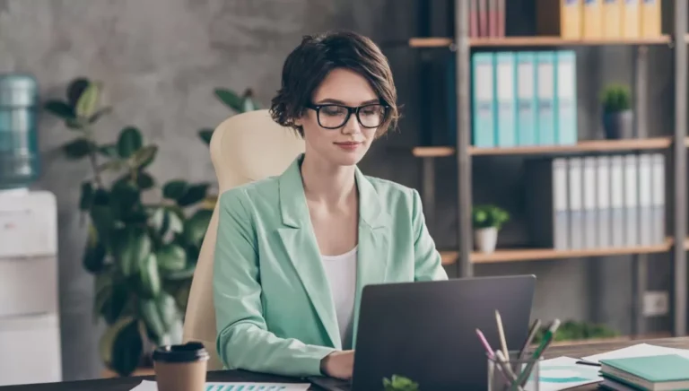 Femme en blazer vert travaillant sur ordinateur portable.