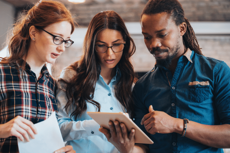 Trois personnes collaborent sur une tablette dans un bureau.
