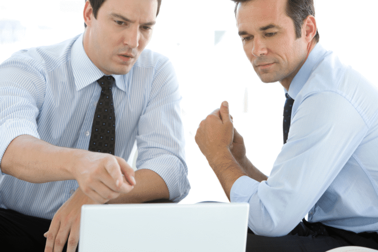 Deux hommes en chemise discutent en consultant un ordinateur portable.