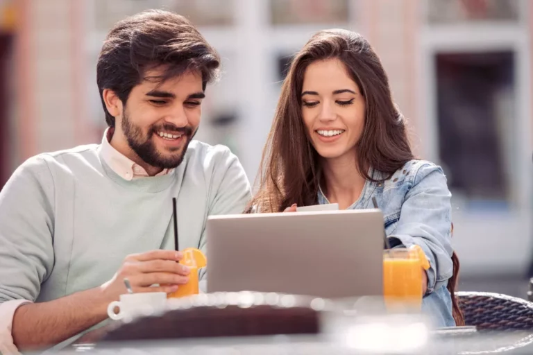 Couple souriant utilisant un ordinateur portable en extérieur.