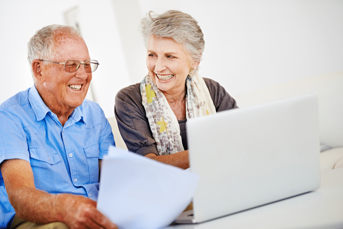 Couple de seniors souriant devant un ordinateur portable.
