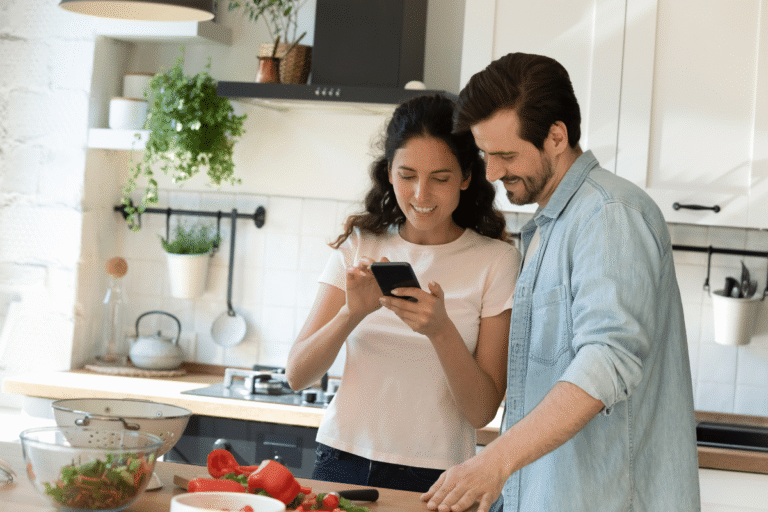 Couple souriant dans une cuisine, consultant un téléphone.