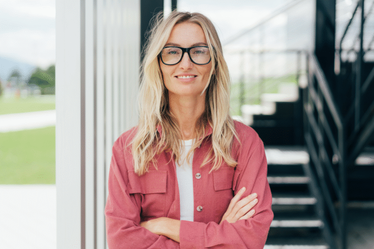 Femme souriante avec cheveux blonds, vêtue d'une chemise rose.